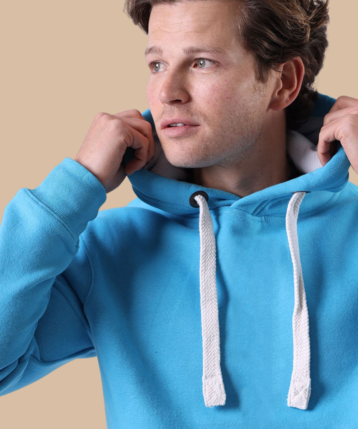 A man wearing a bright blue pullover hoodie with white drawstrings, adjusting the hood against a solid beige background. Pathfinder Printworks hand print apparel for clubs, teams and businesses.