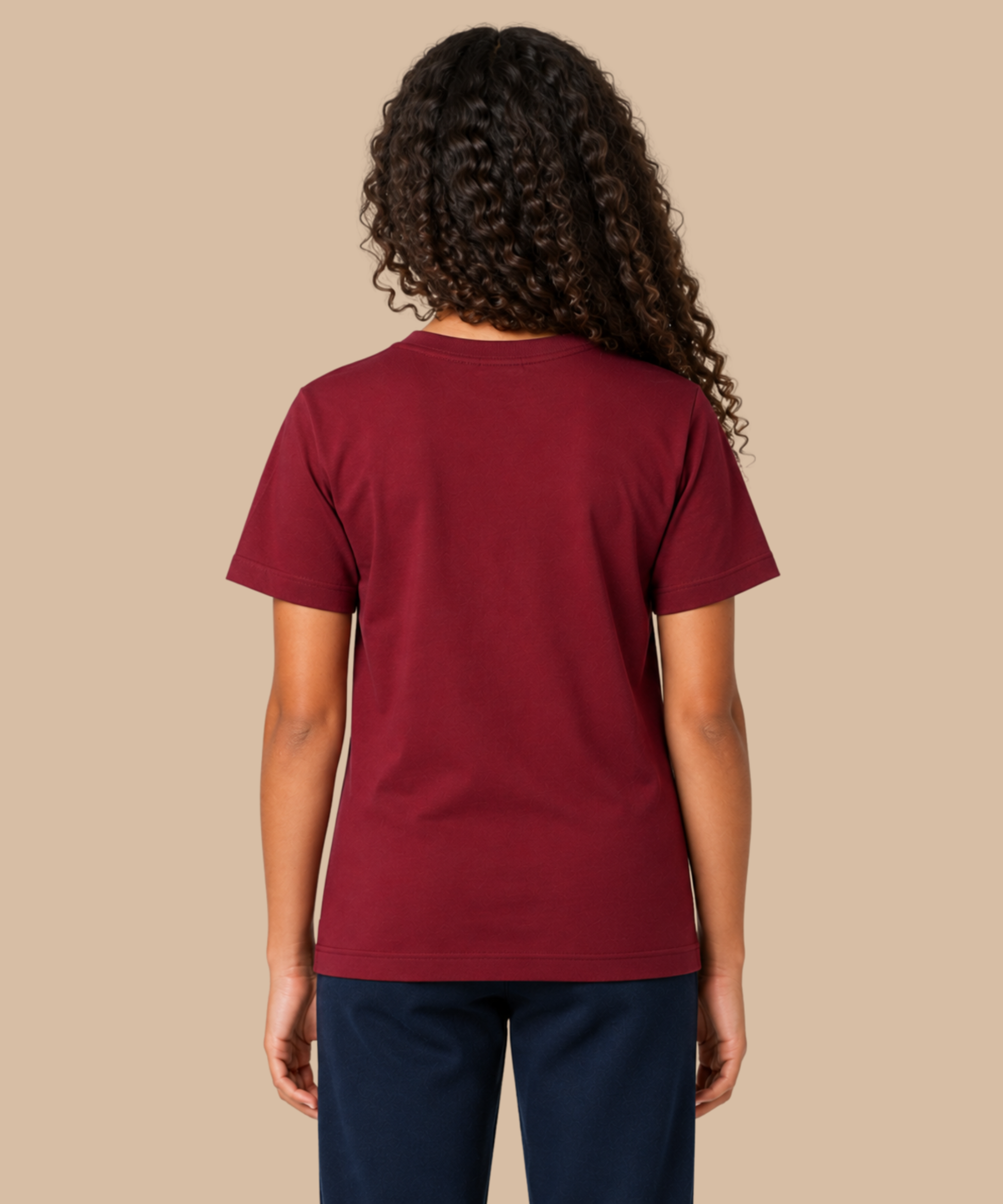 A person shown from the back wearing a short-sleeve crewneck t-shirt in burgundy and dark navy pants, set against a solid beige background. Handprinted t-shirt services from Pathfinder Printworks.