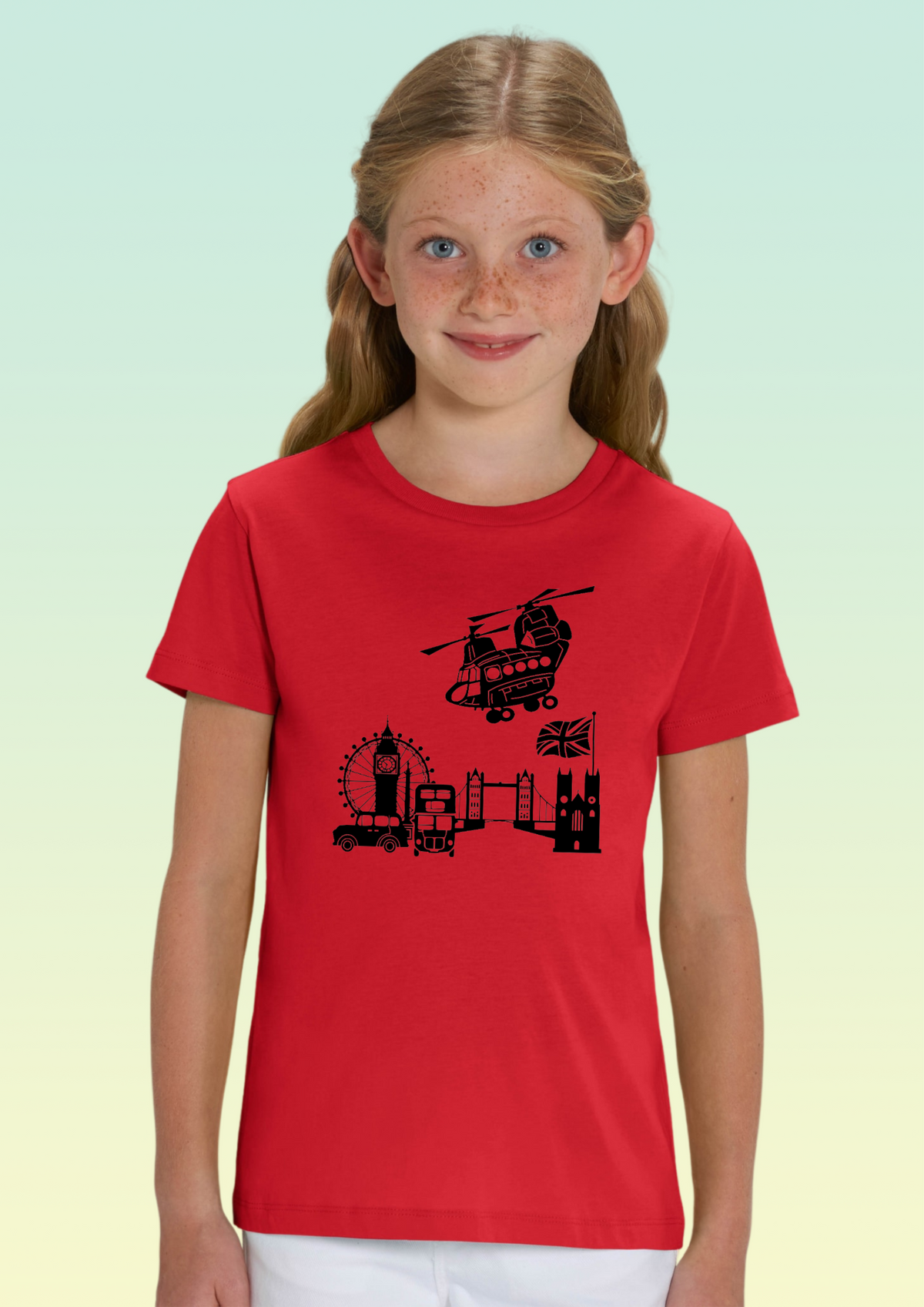 A young girl with freckles modeling a red short-sleeve t-shirt featuring a black graphic of London landmarks, including Big Ben, the London Eye, and a helicopter, against a light green gradient background. Exclusive to Flying Teez.