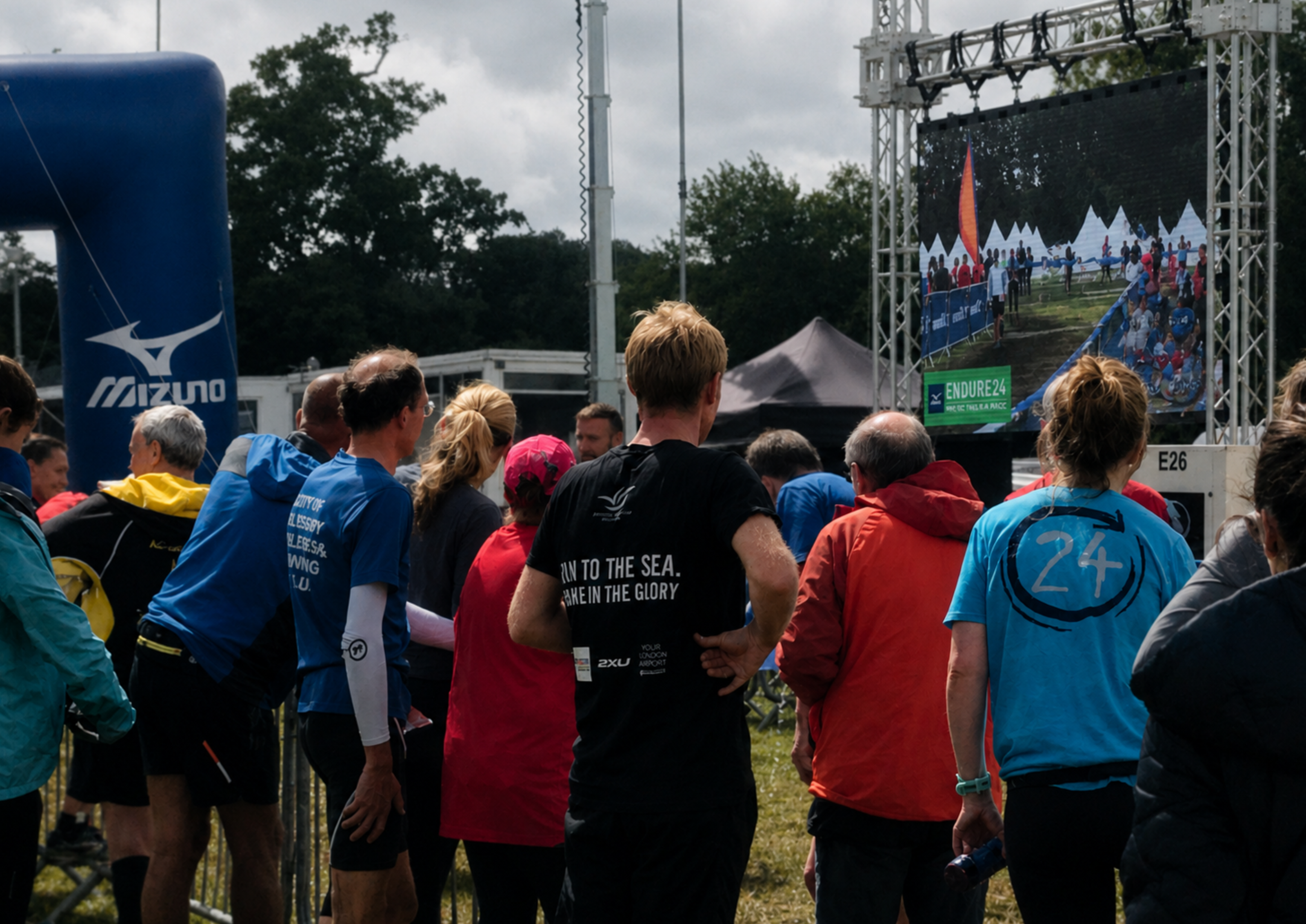 Group of people gathered at Endure 24 trail running event with a large screen displaying graphics. Pathfinder Printworks hand print t-shirts and hoodies for all types of events.