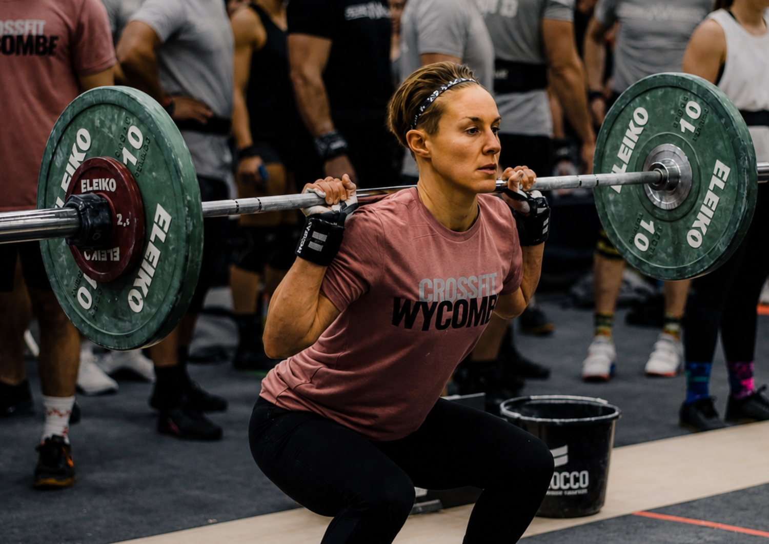 An athlete wearing a branded CrossFit vest competes in a strength event, lifting heavy weights. The image captures determination, focus and the demands of high-performance team sport.
