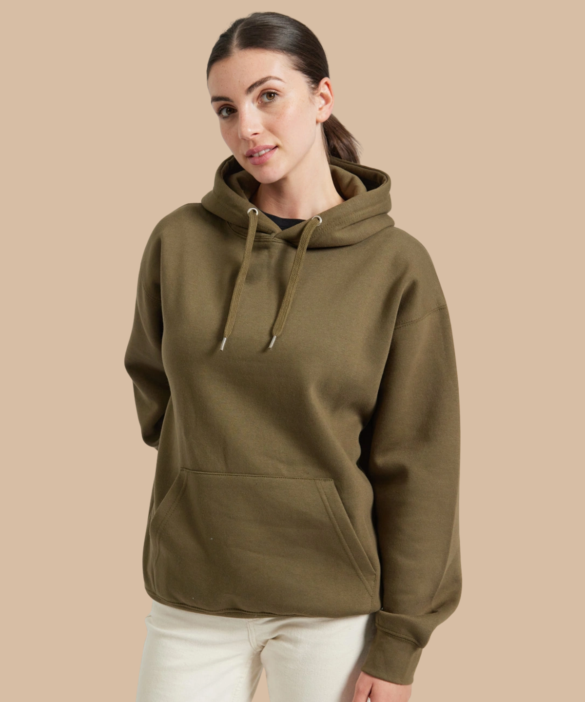 A woman wearing an olive green pullover hoodie with a front kangaroo pocket and drawstrings, paired with white pants, set against a solid beige background. Pathfinder Printworks hand print for clubs, teams and businesses. 