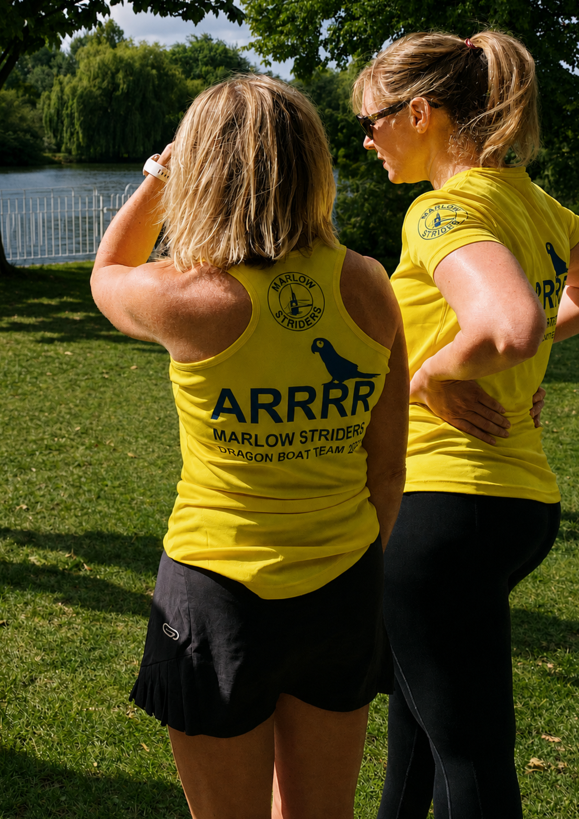 Two women in yellow shirts with 'ARRRR Marlow Striders Dragon Boat Team' text standing outdoors by the River Thames.