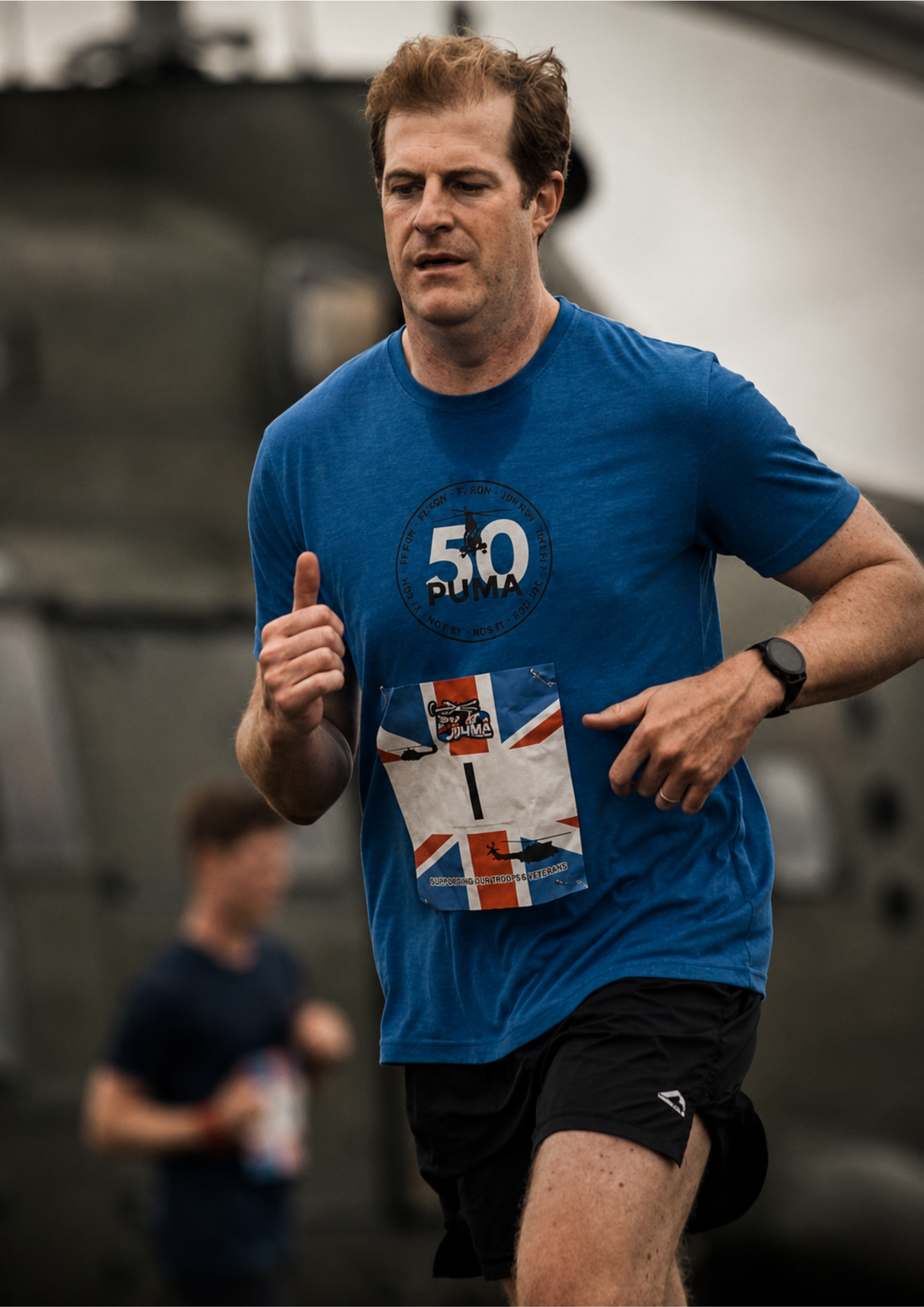 Runner wearing a blue event t-shirt and race number during a challenge event. The portrait captures determination and focus mid-run, with a shallow depth of field creating separation from the background.