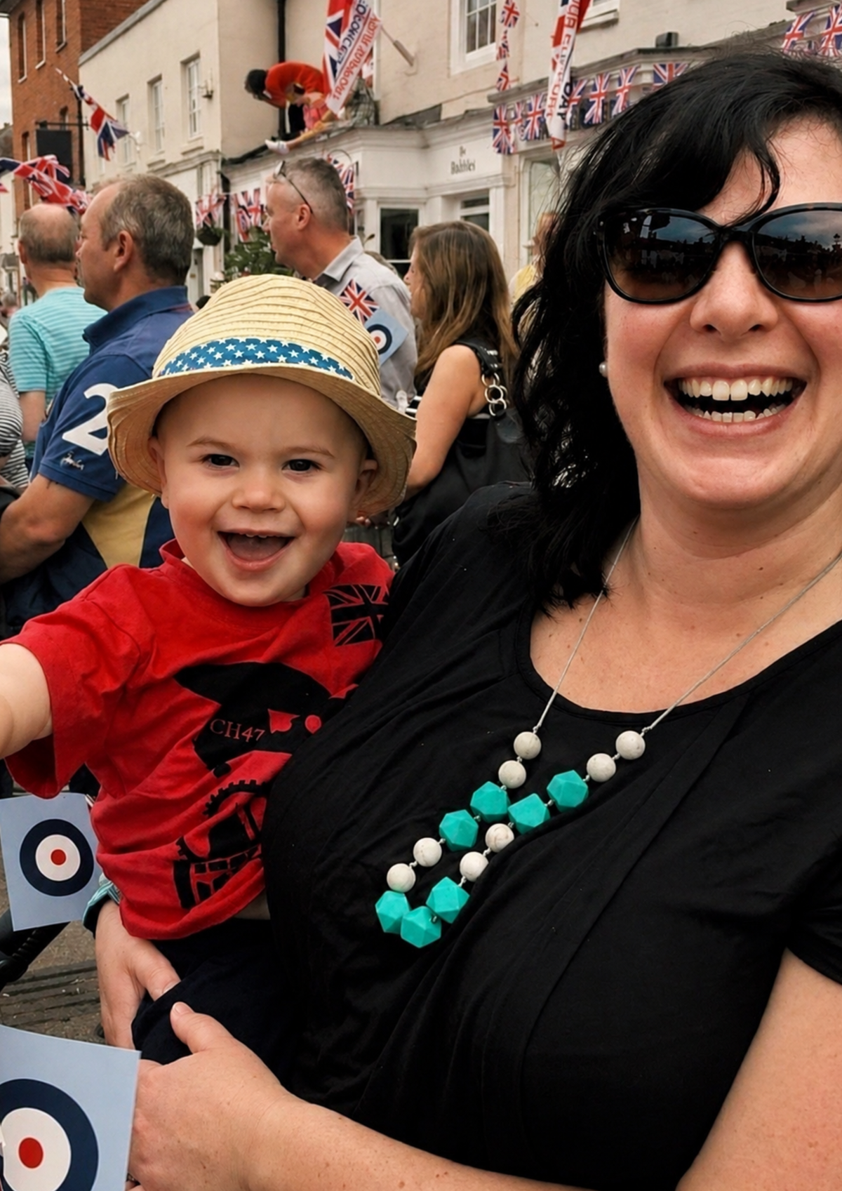 Woman holding a child with a festive background featuring flags and buildings.
