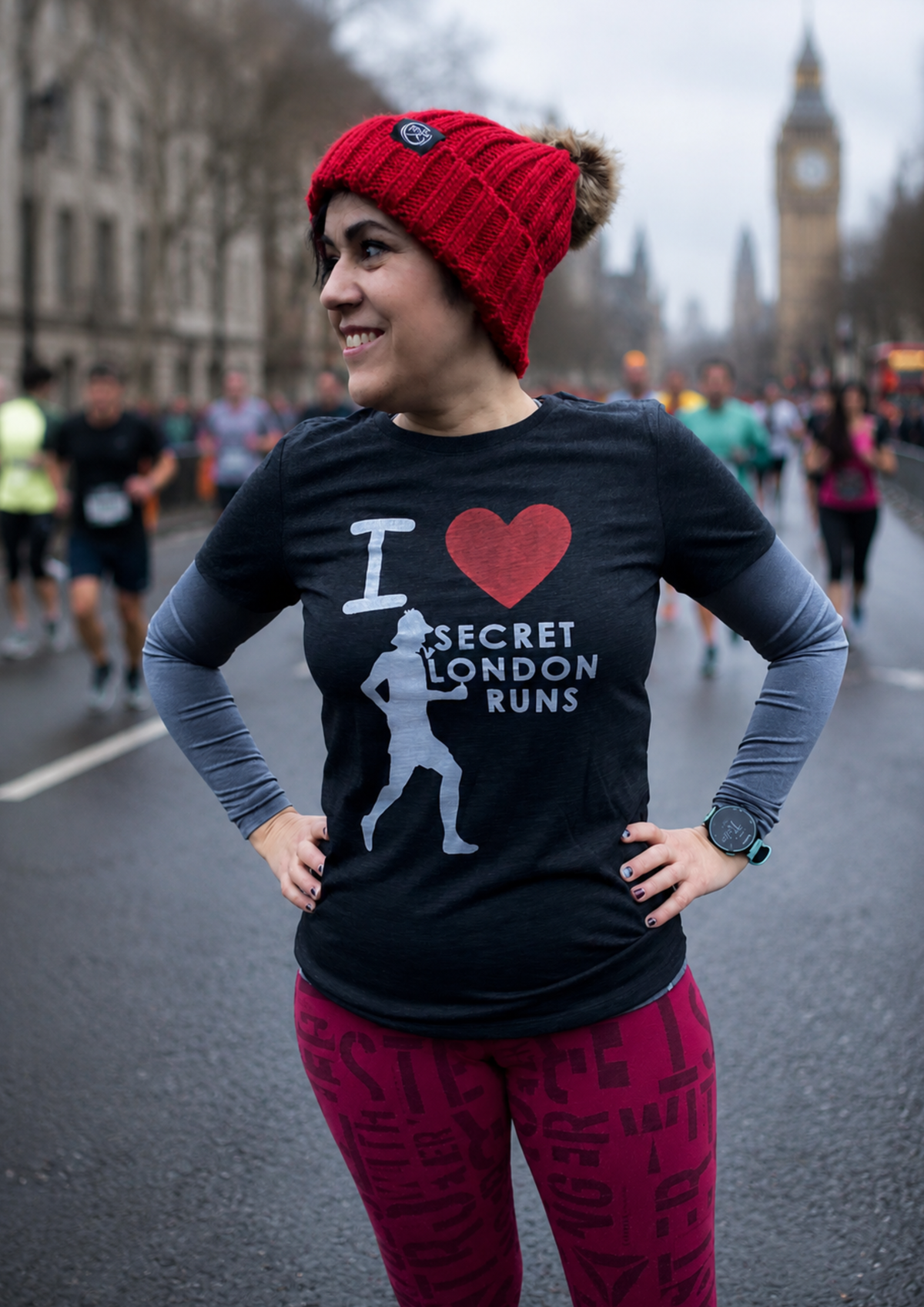Runner wearing a red bobble hat and black Secret London Runs t-shirt standing on a closed London street during a race event, with Big Ben visible in the background.