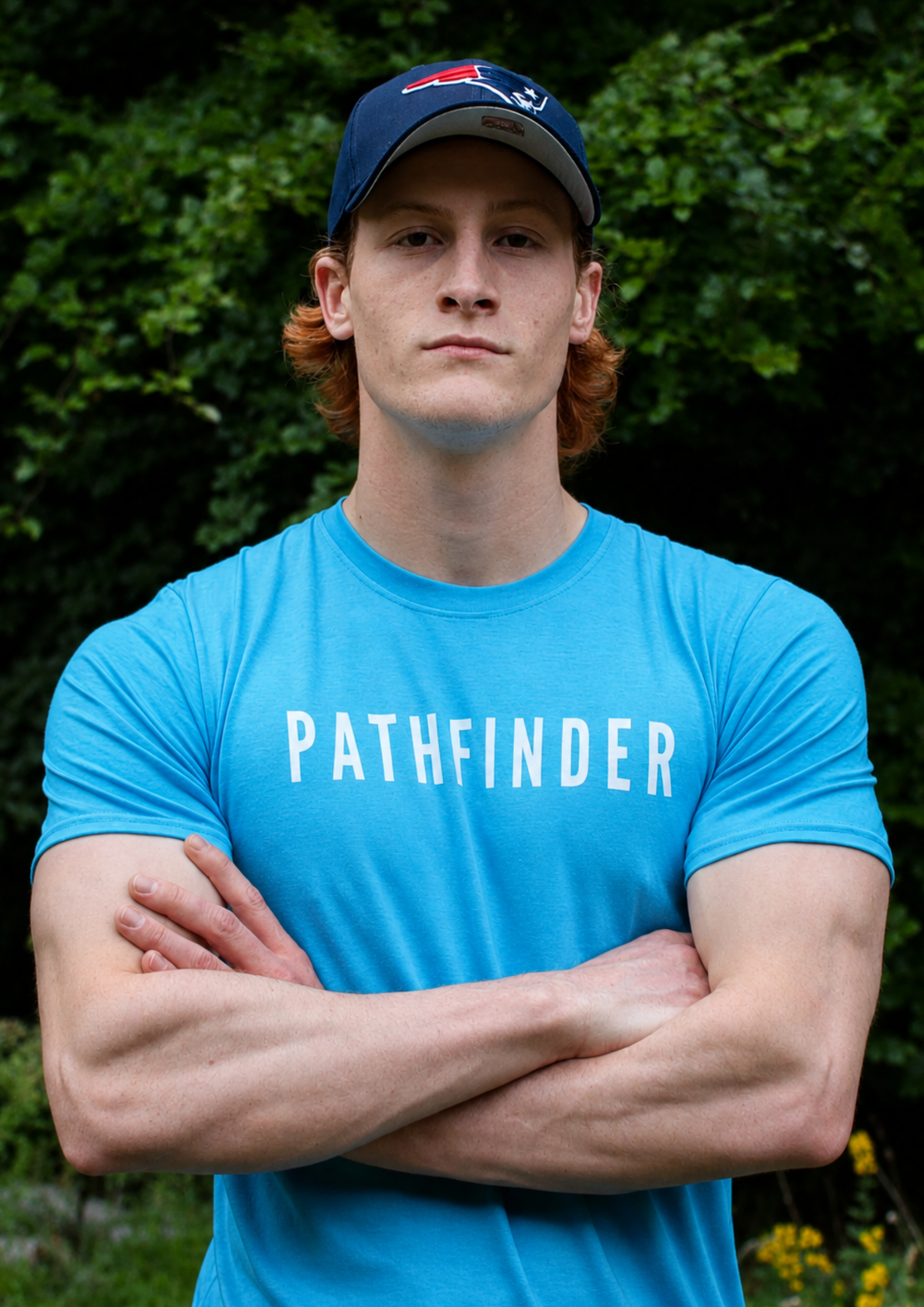 Young man standing with arms folded wearing a light blue Pathfinder t-shirt against a dark woodland background.
Pathfinder Printworks hand print apparel for clubs, teams and businesses.