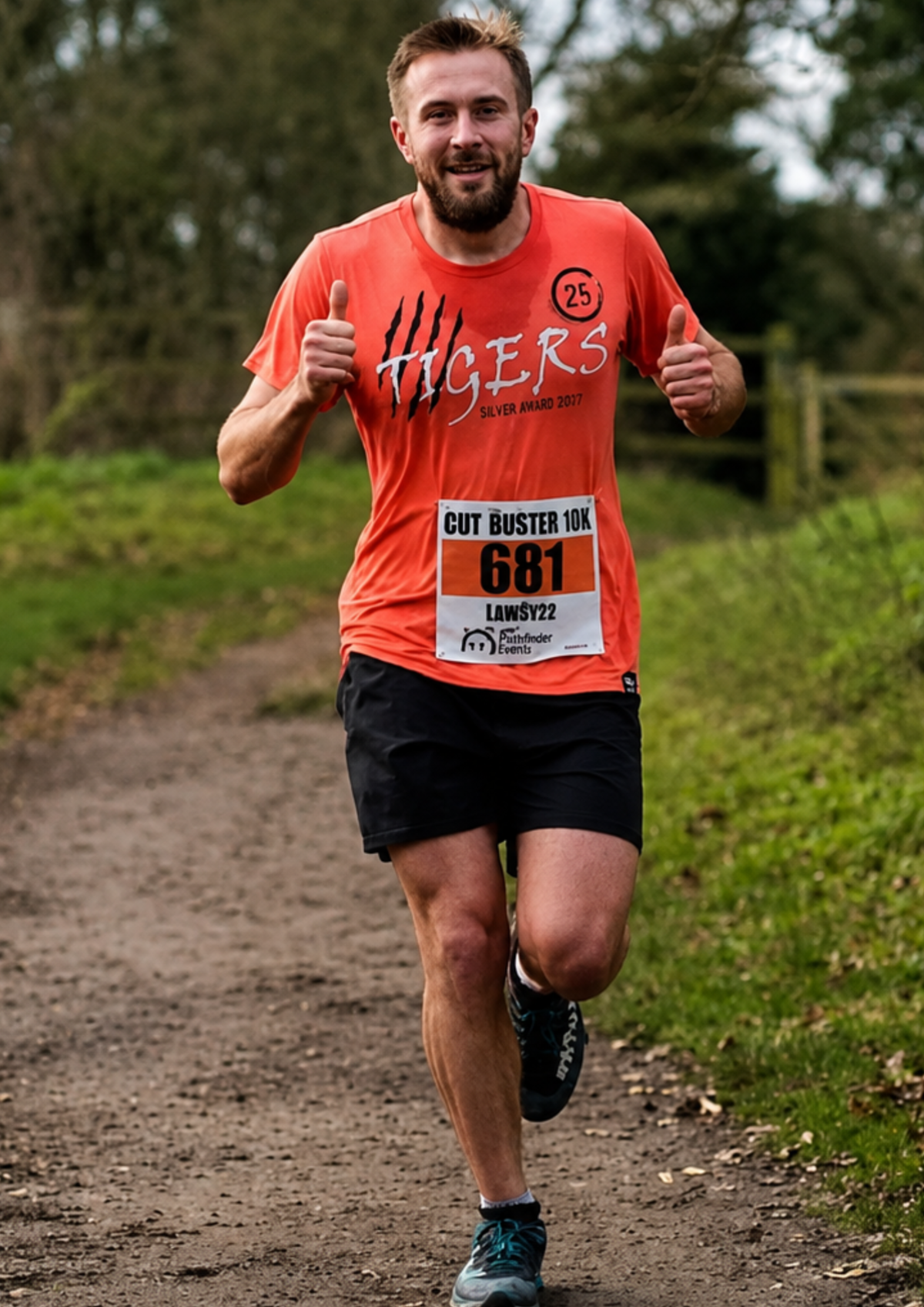 Man running outdoors on a dirt path wearing an orange t-shirt with 'Tigers' printed on it.