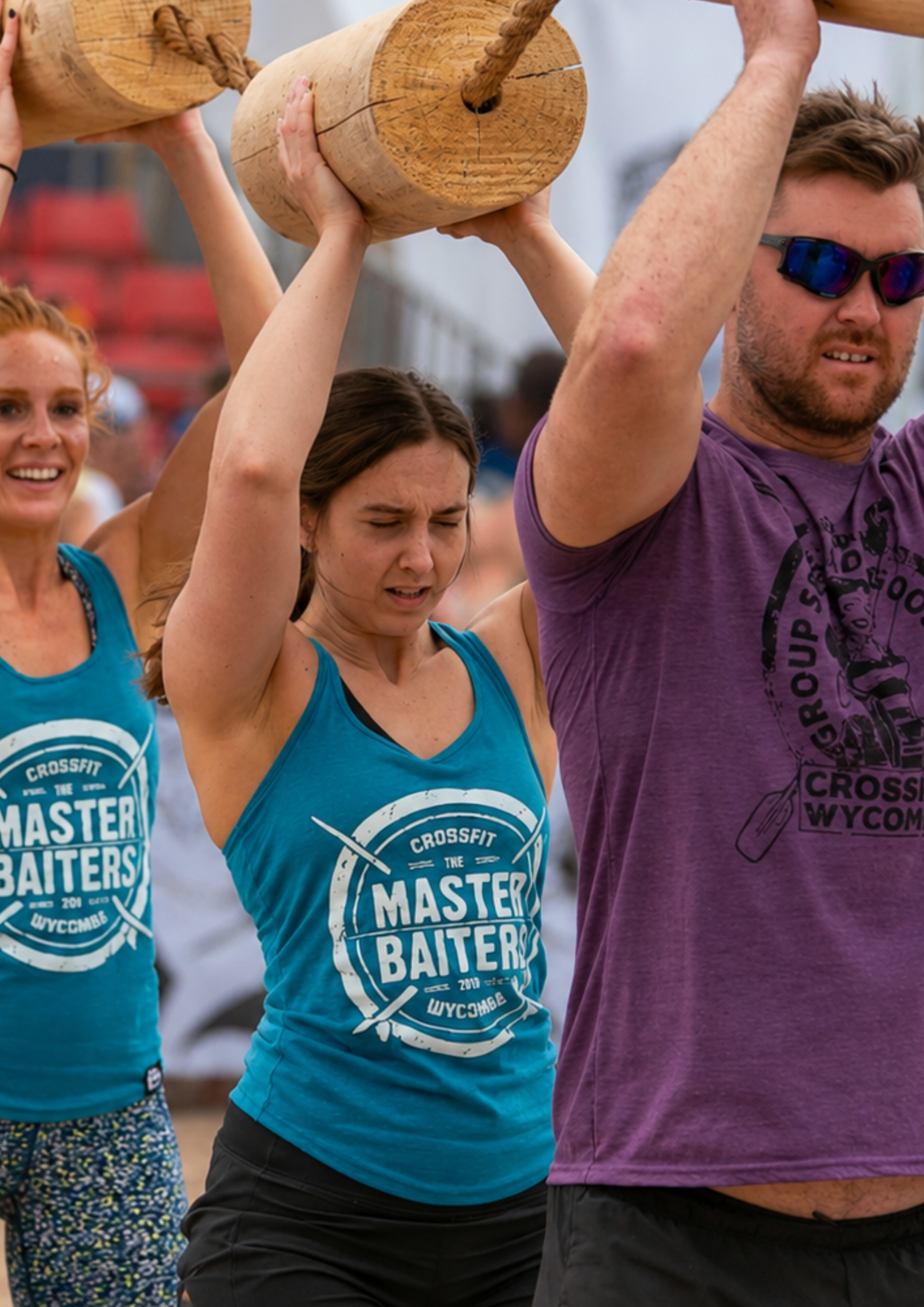 A team works together to carry a heavy sandbag across a beach challenge course while wearing branded apparel. The image represents shared responsibility, teamwork and the importance of supporting one another to achieve a common goal.