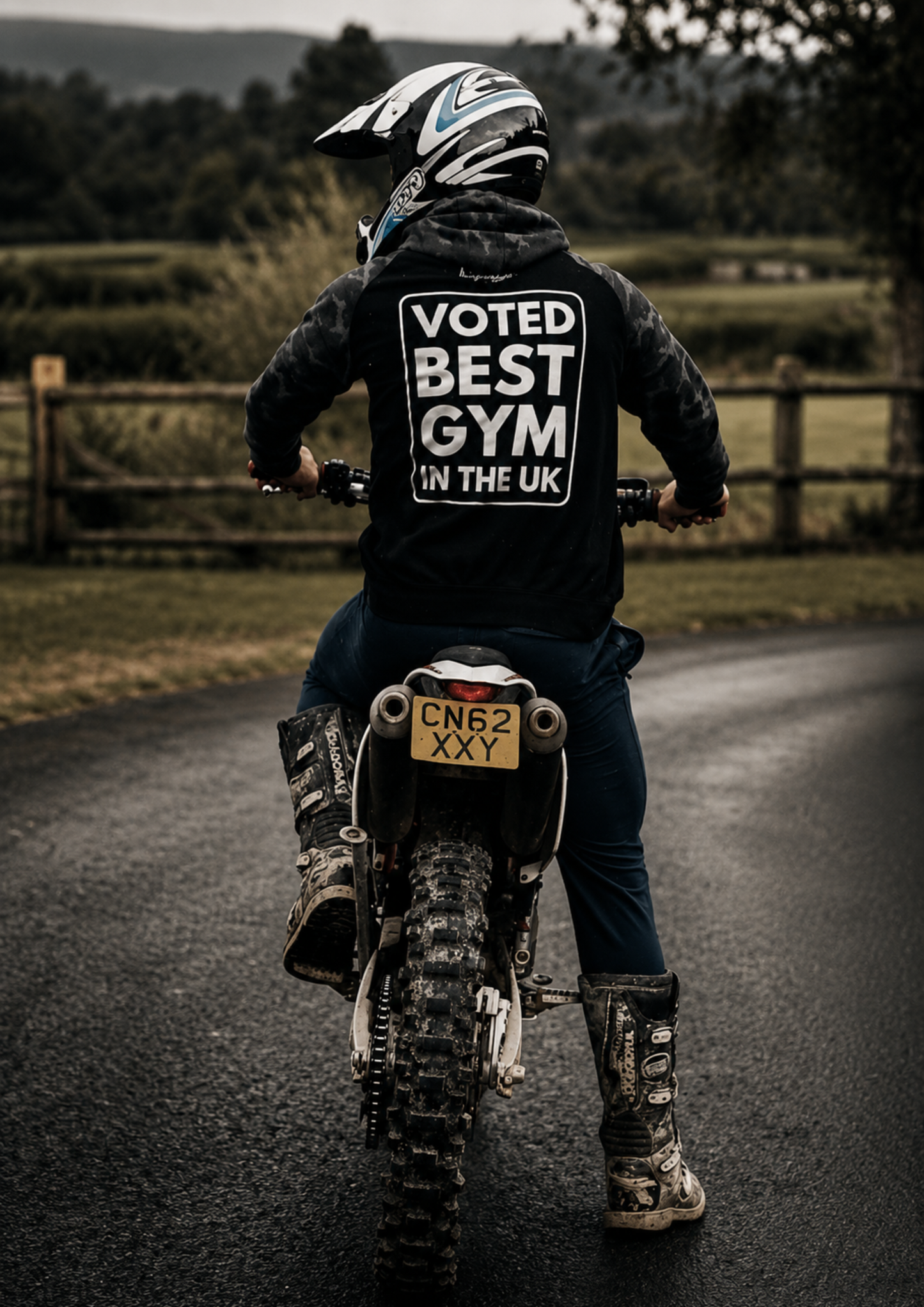 Motorcyclist wearing a branded hoodie while sitting on an off-road motorcycle on a country road. The large back print is clearly visible, demonstrating how custom apparel can extend beyond training environments into everyday adventures.