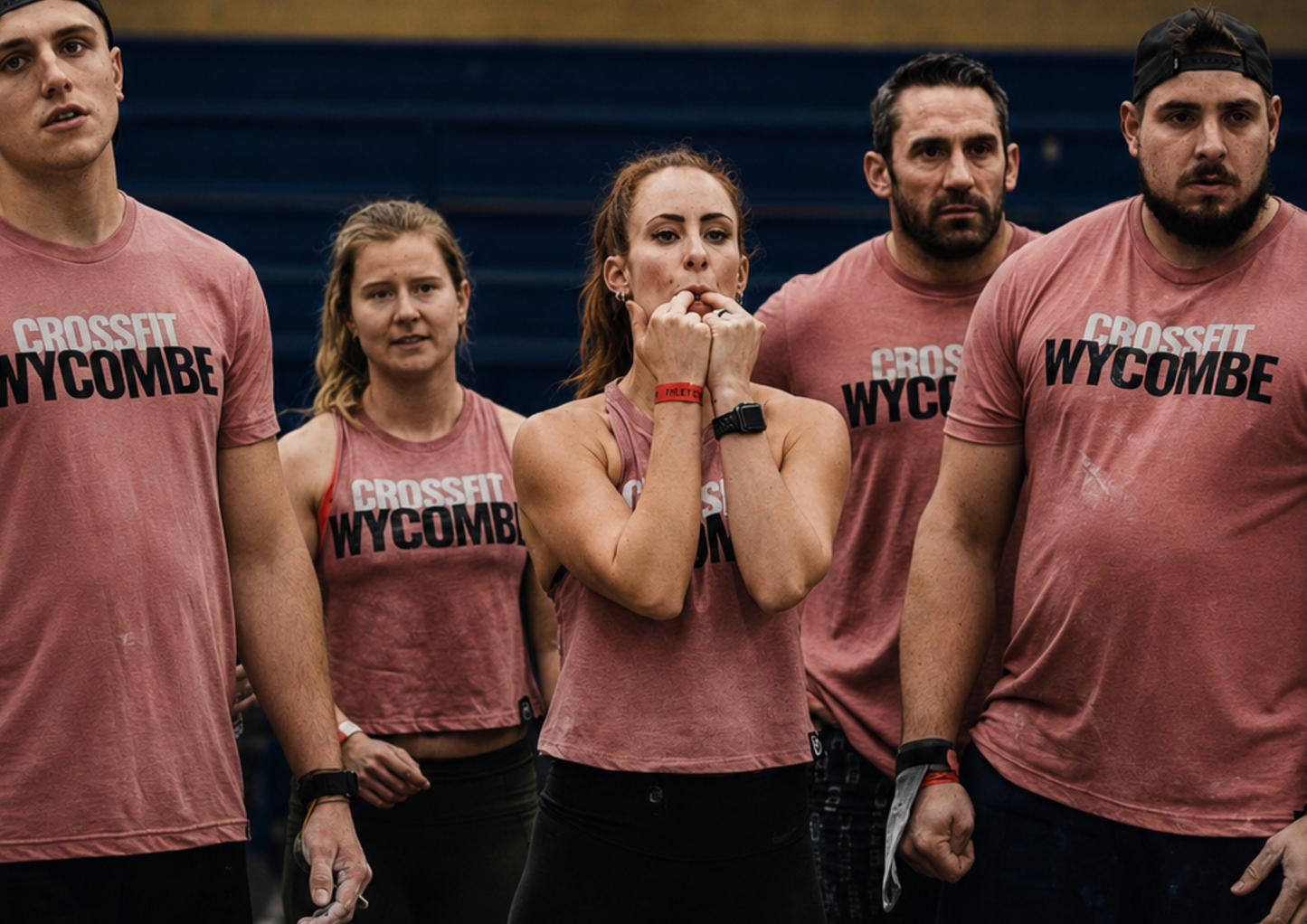 A group of CrossFit athletes wearing matching team apparel watch an event intently during a fitness competition. Their focused expressions highlight the support, anticipation and shared investment that exist within a strong team environment.