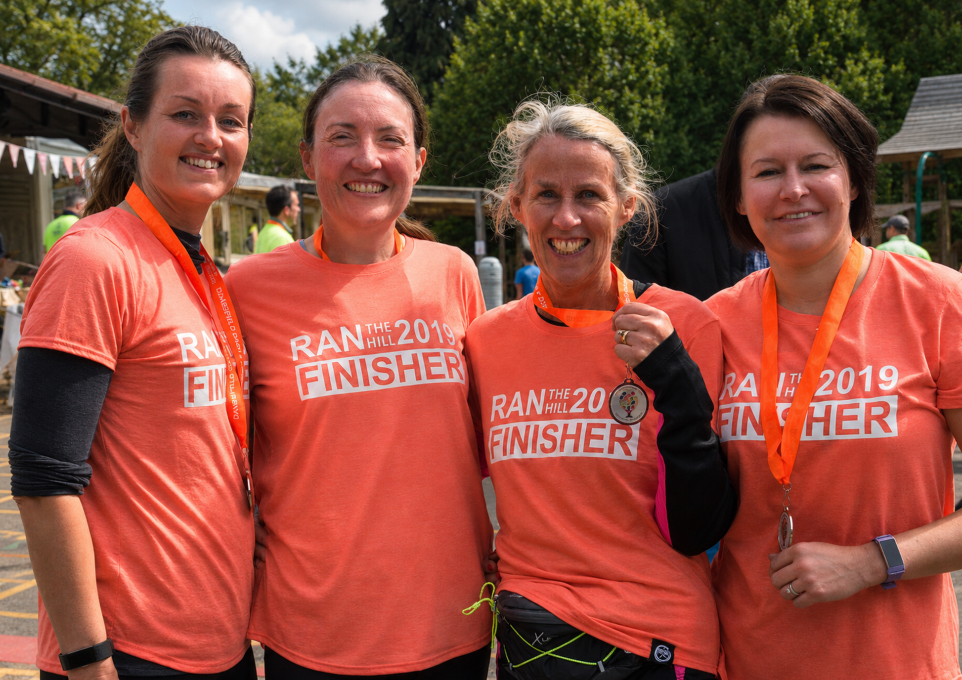 Four participants stand together smiling after completing an event, wearing matching finisher t-shirts and medals. The image captures pride, achievement and the shared sense of accomplishment that comes from reaching a goal together.