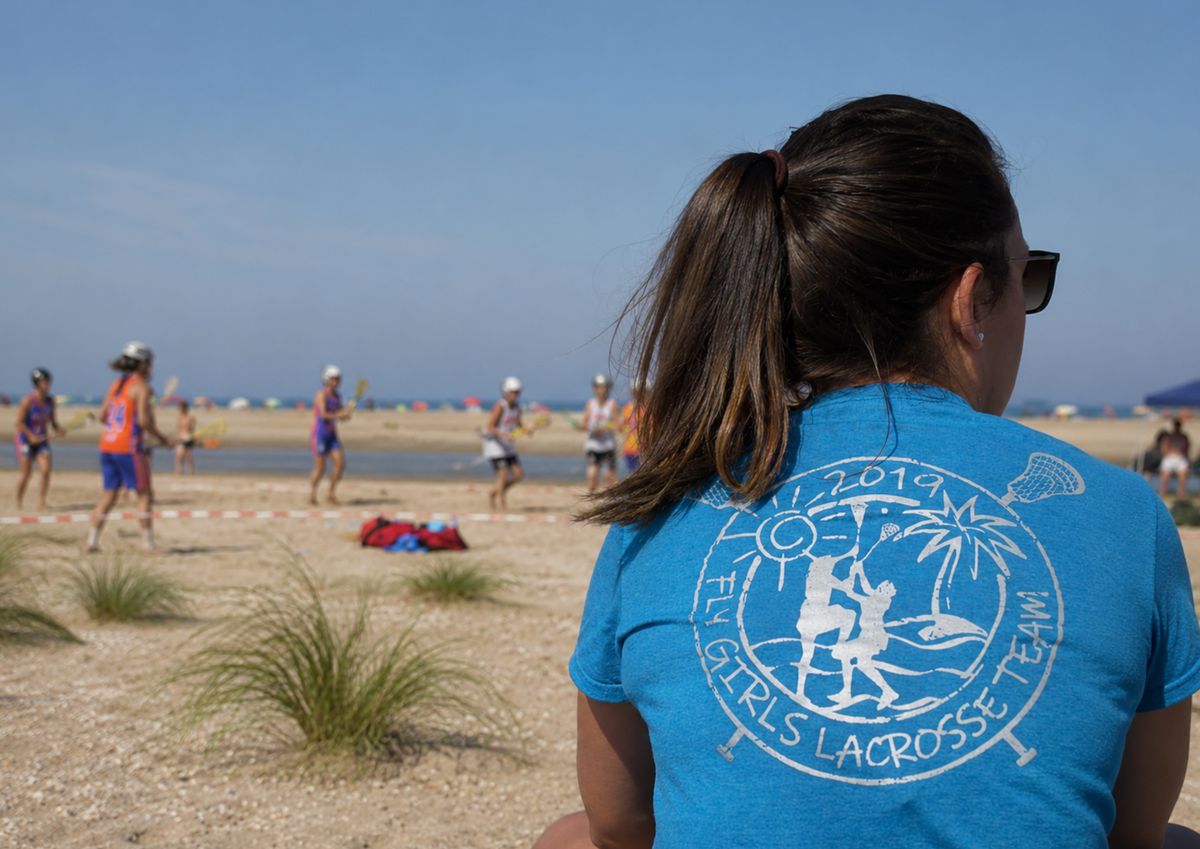 A supporter wearing a branded team shirt watches a sporting event taking place on a beach in the background. The image highlights support, community involvement and the important role played by those behind the scenes.