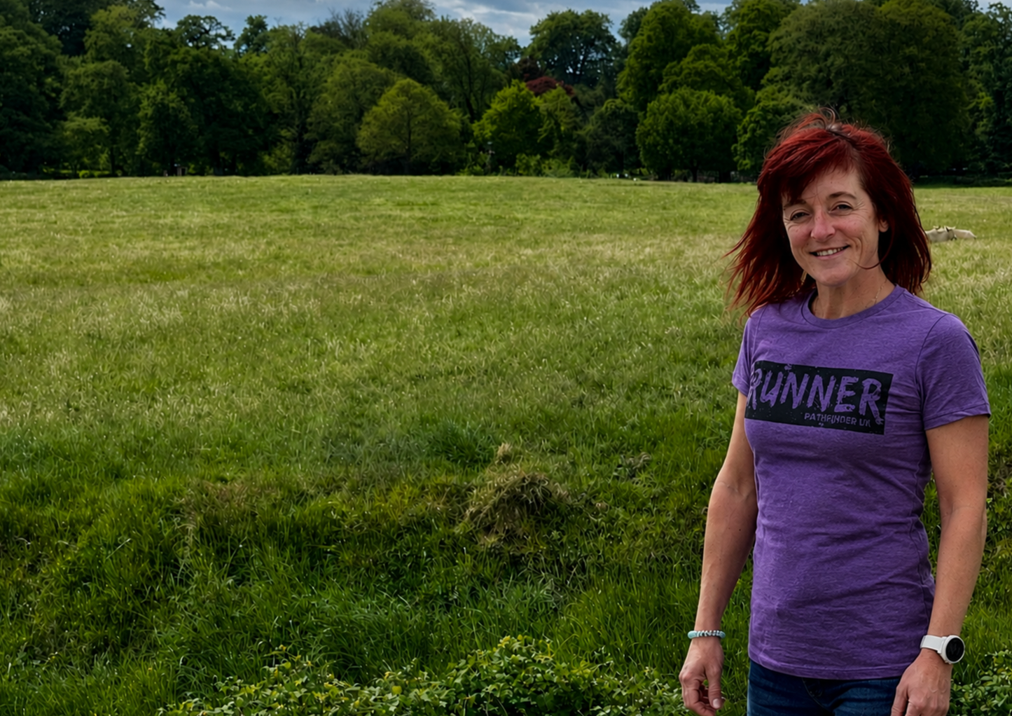 Person wearing a purple 'RUNNER' t-shirt standing in a grassy field with trees in the background. Hand printed apparel for teams, clubs and businesses.