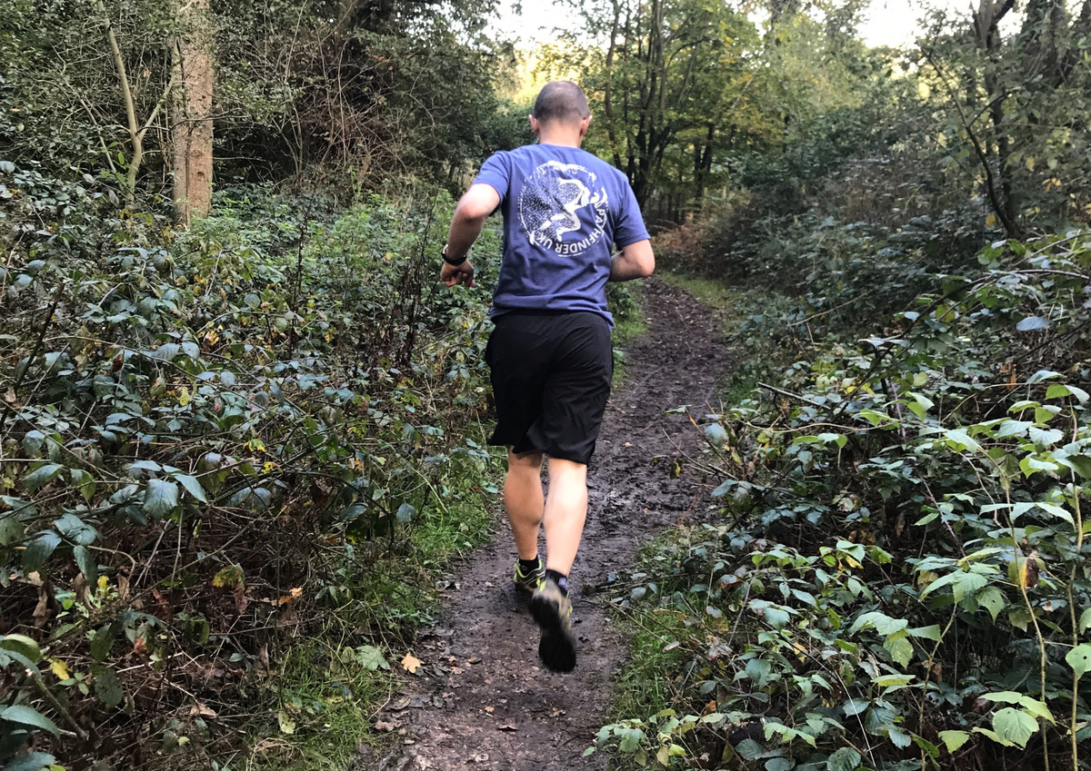 Man running on a forest path surrounded by greenery, wearing a Pathfinder UK hand printed t-shirt with a runner graphic. Screen printed by Pathfinder Printworks in South Wales.