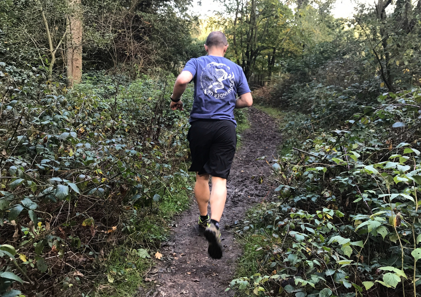 Man running on a forest path surrounded by greenery, wearing a Pathfinder UK hand printed t-shirt with a runner graphic. Screen printed by Pathfinder Printworks in South Wales.