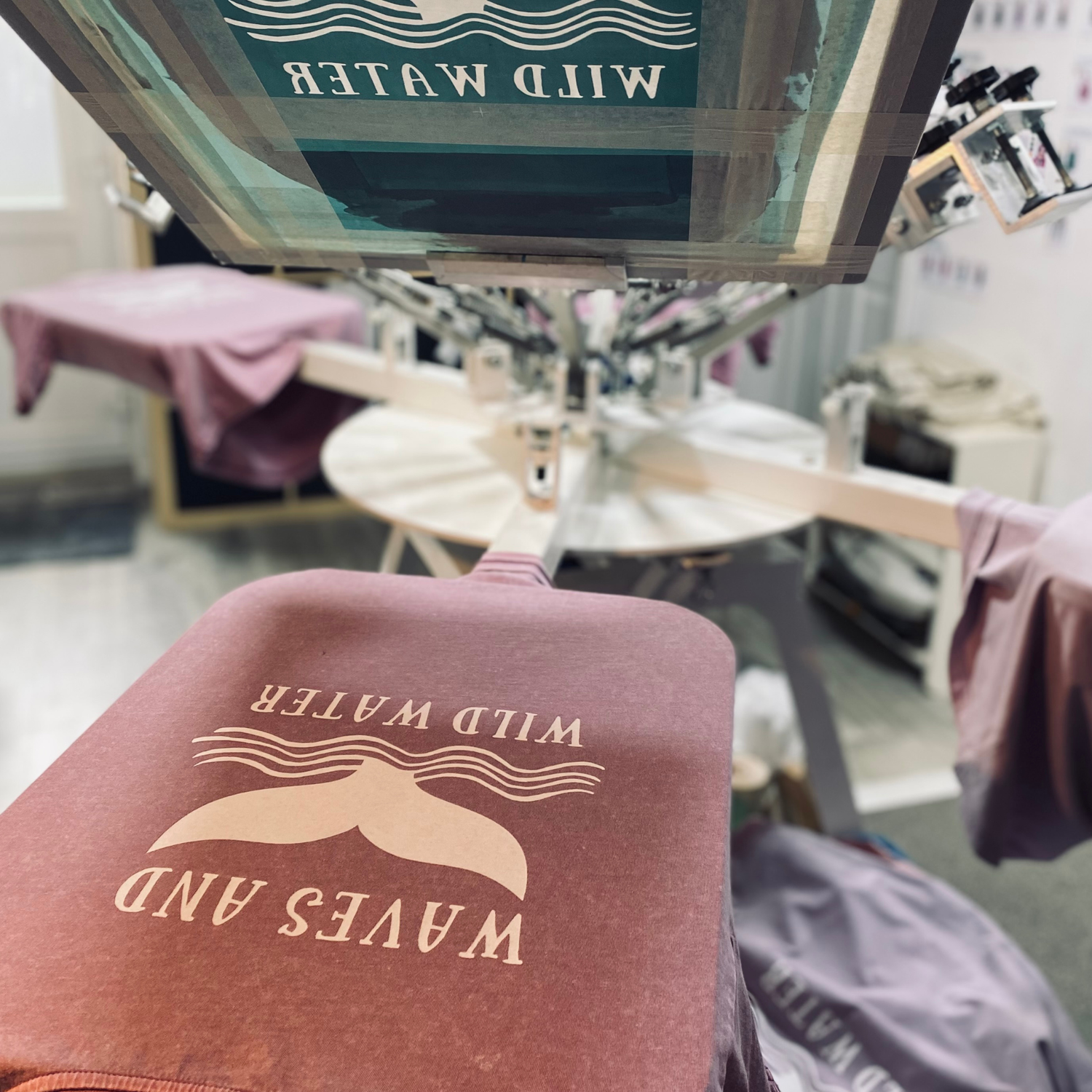 T-shirt with 'Wild Water Waves and' text on a printing press in a garment factory setting. Pathfinder Printworks hand screen print clothing for club, teams and businesses.