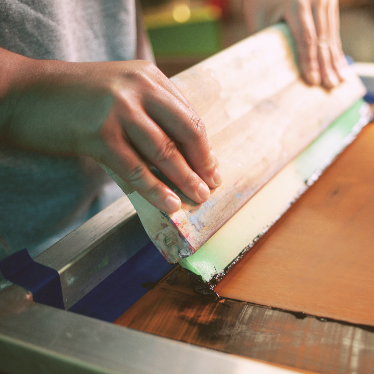 A close-up of a person's hands using a squeegee to transfer a printed design onto a t-shirt. Pathfinder Printworks hand screen print for clubs, teams & businesses.