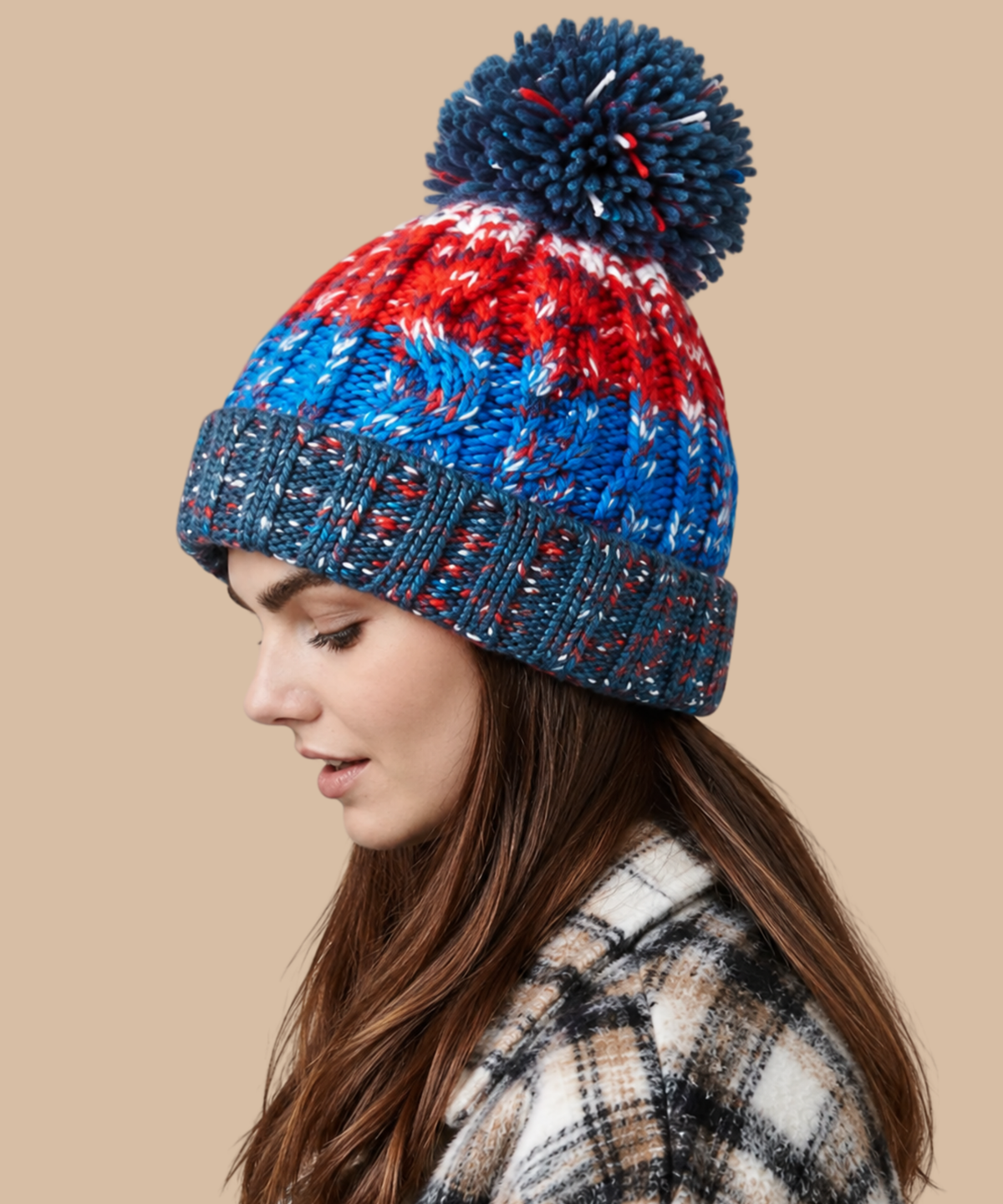 A woman in profile wearing a chunky knit winter hat with a large pom-pom. The hat features horizontal stripes of red, blue, and navy with white flecks, and a ribbed navy cuff. Pathfinder Printworks offer embroidery services to teams, clubs and businesses.