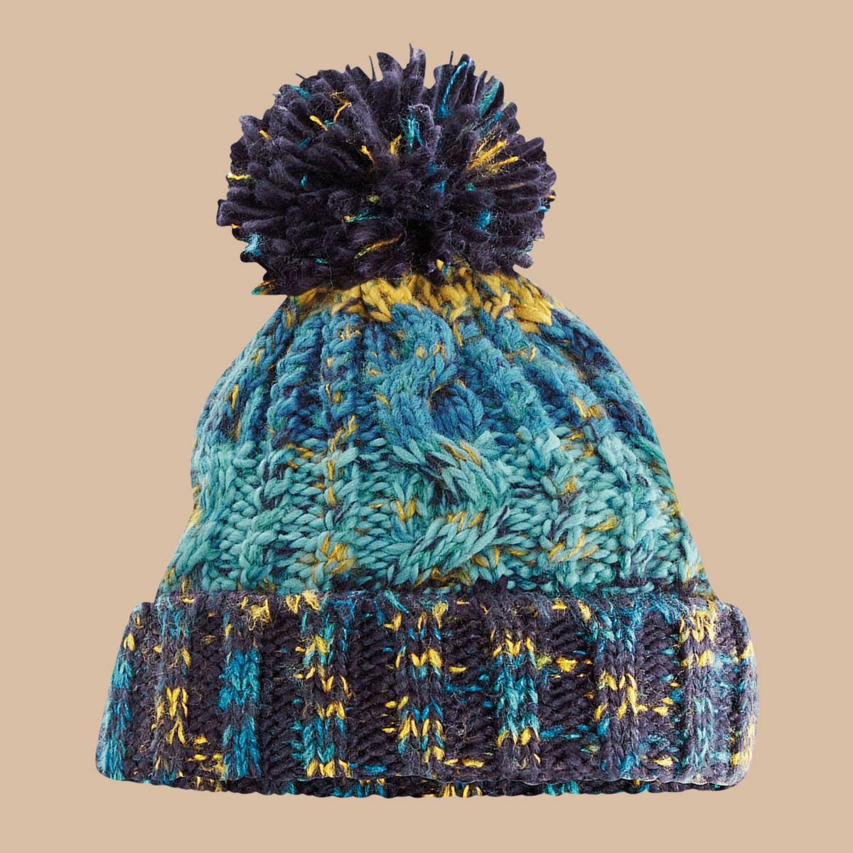 A marled knit pom-pom beanie hat featuring a teal and navy cable knit pattern with yellow accents, set against a solid beige background. Embroidery services from Pathfinder Printworks, based in South Wales.