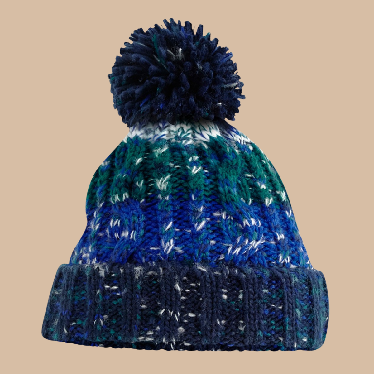 A marled knit beanie hat with a large pom-pom, featuring horizontal bands of navy, blue, green, and white yarn, set against a solid beige background. Embroidery services from Pathfinder Printworks, based in South Wales.