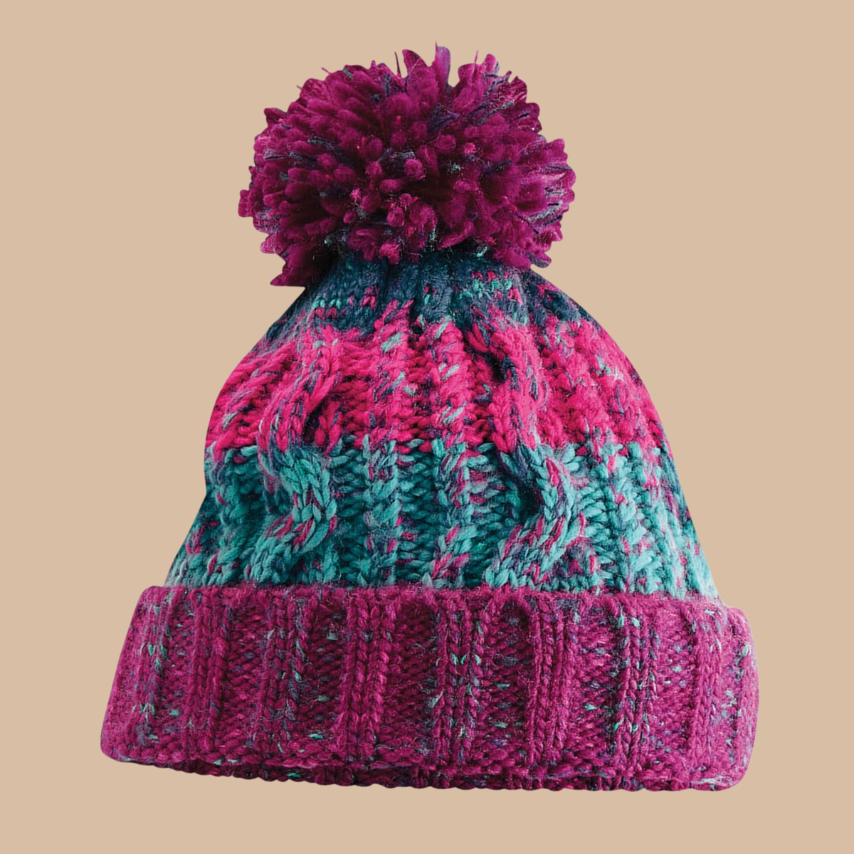 A marled cable-knit beanie hat with a large pom-pom, featuring stripes of magenta pink, teal green, and dark navy blue, set against a solid beige background. Embroidery services from Pathfinder Printworks, based in South Wales.