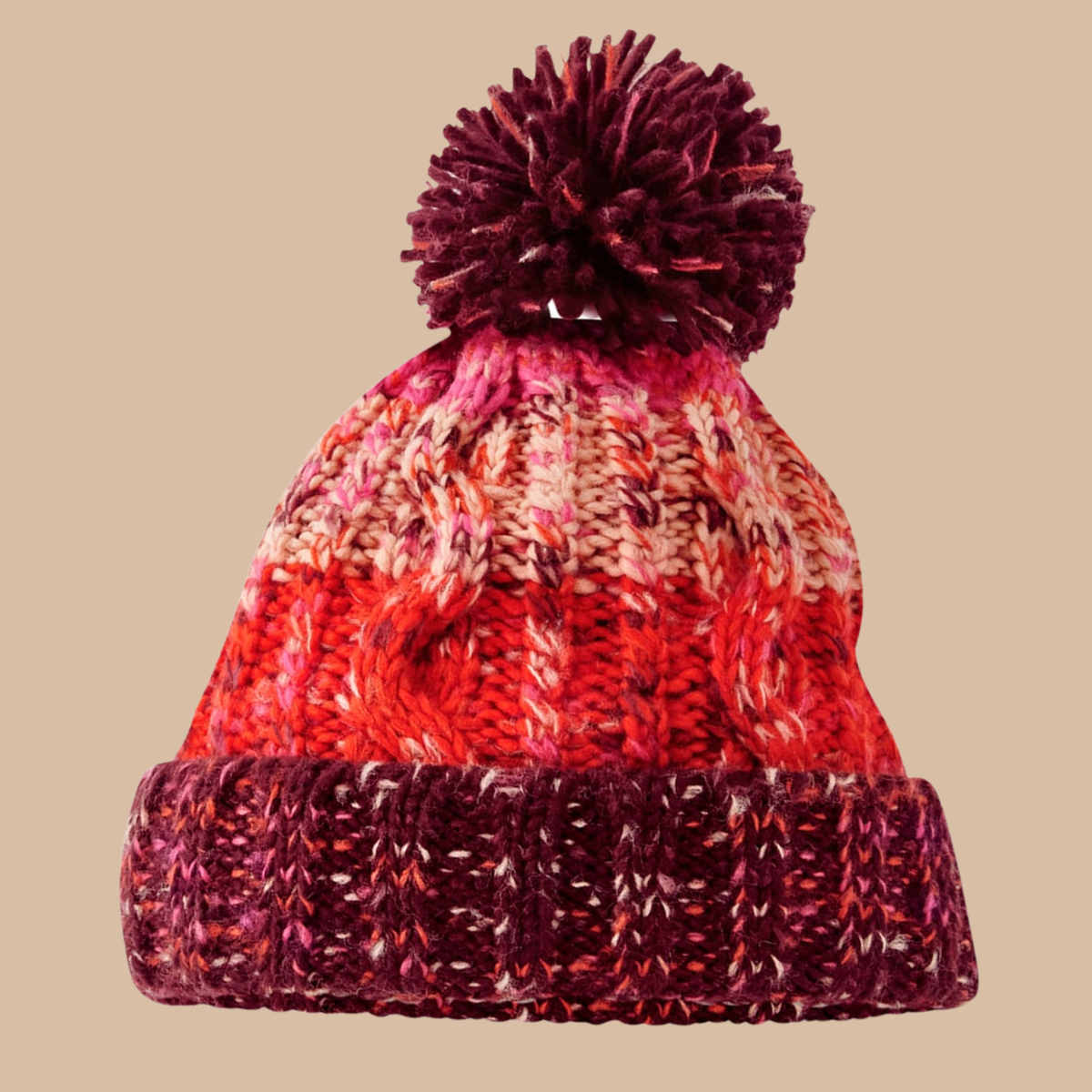 A marled knit pom-pom beanie hat featuring a gradient of red, orange, pink, and deep burgundy yarn, set against a solid beige background. Embroidery services from Pathfinder Printworks, based in South Wales.