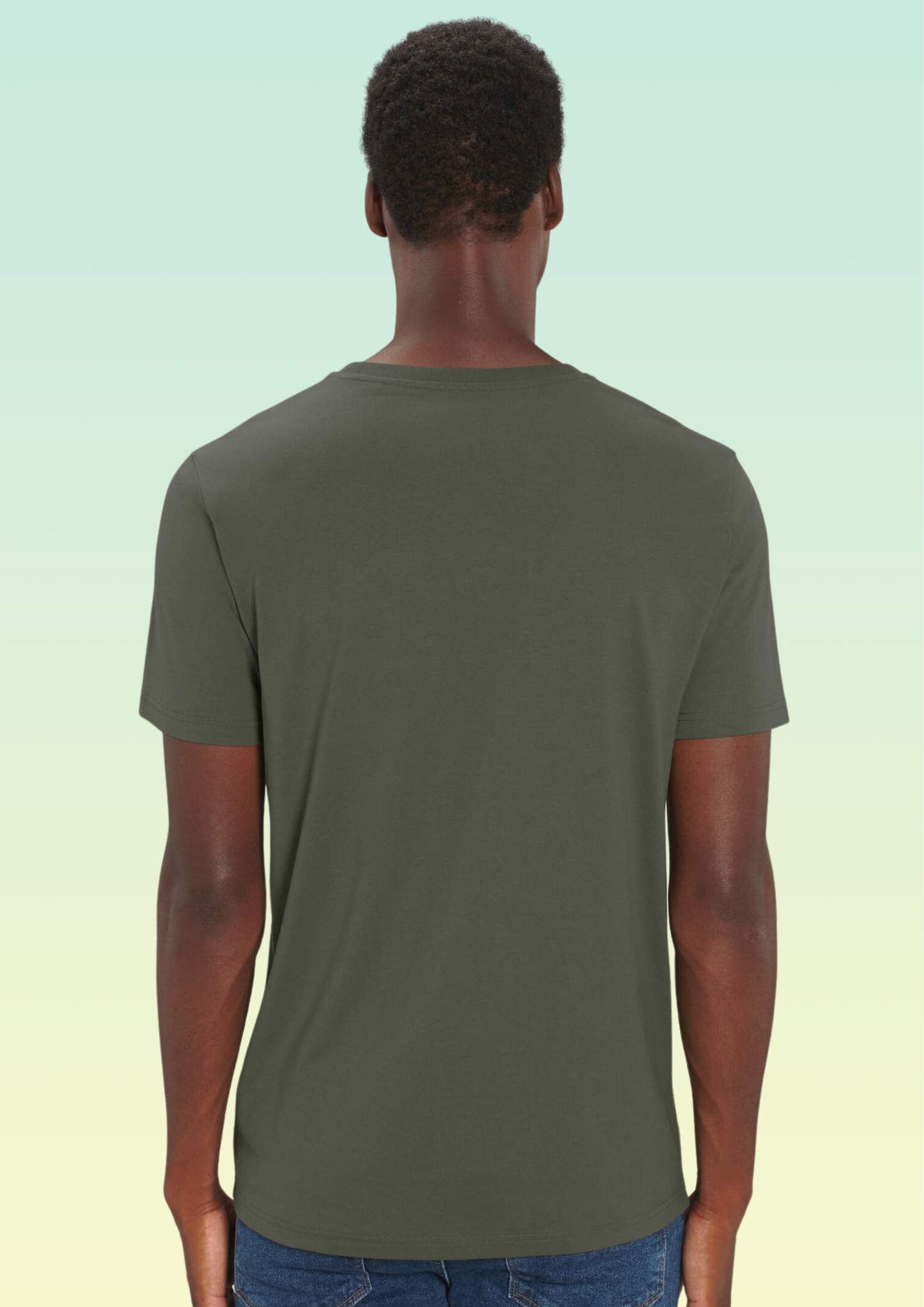 A man viewed from the back wearing a solid olive green short-sleeve t-shirt and blue jeans, set against a light green to pale yellow gradient background. Exclusive to Flying Teez.